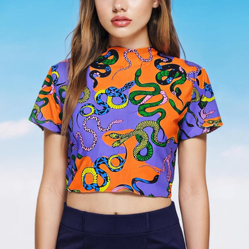 A vibrant see-through mesh crop top with a high mock neck and short sleeves. The shirt features a bold, all-over snake print pattern with colorful green, blue, yellow, and black serpents on a striking orange and purple color-block background. This Y2K-style top is a statement piece of witchy, goth, and alternative clothing, perfect for a maximalist rave outfit or edgy festival fashion from a black owned shop.